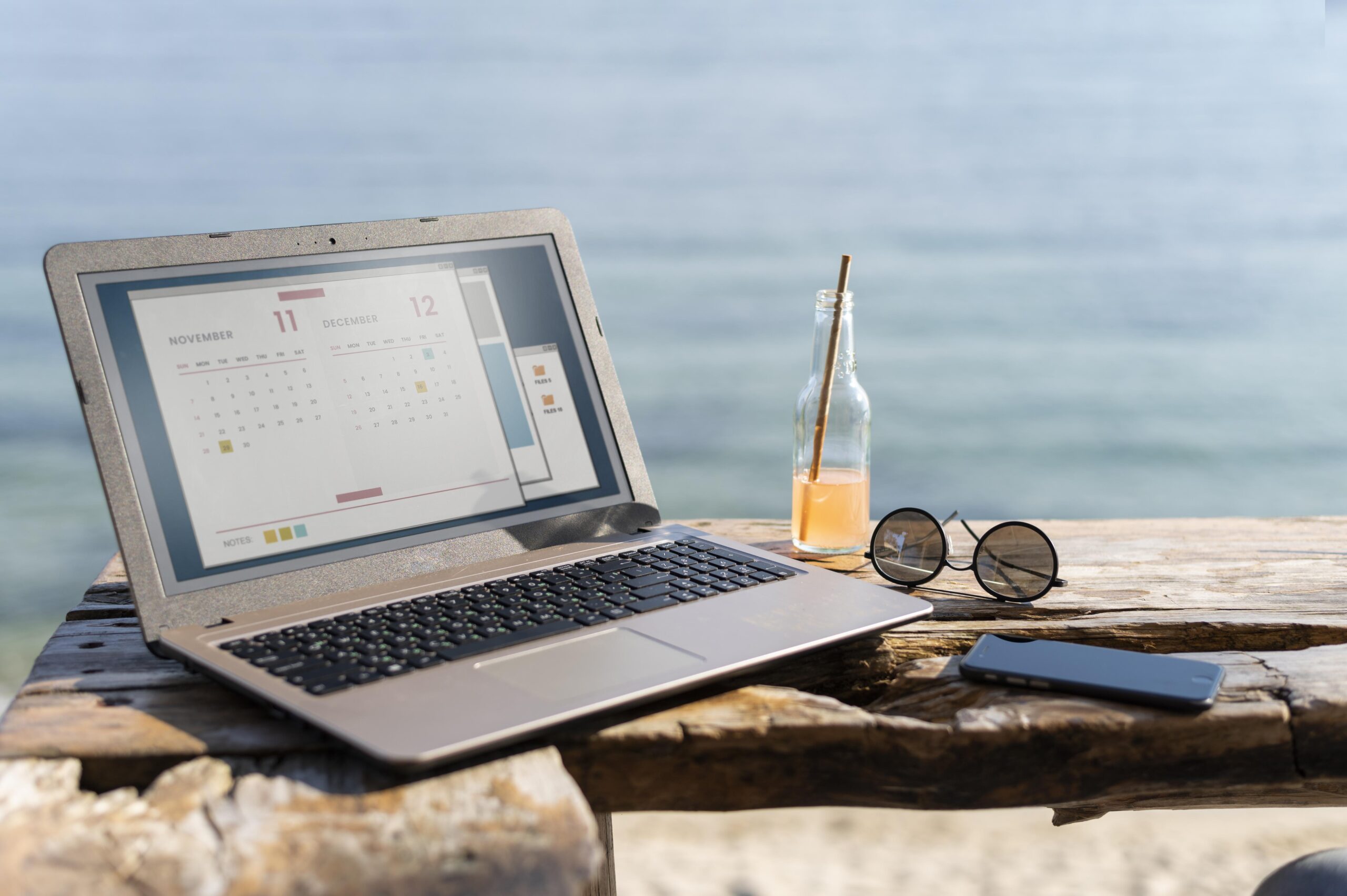 Zomerse foto van laptop met een planning erop in de zon, met een zonnebril er naast