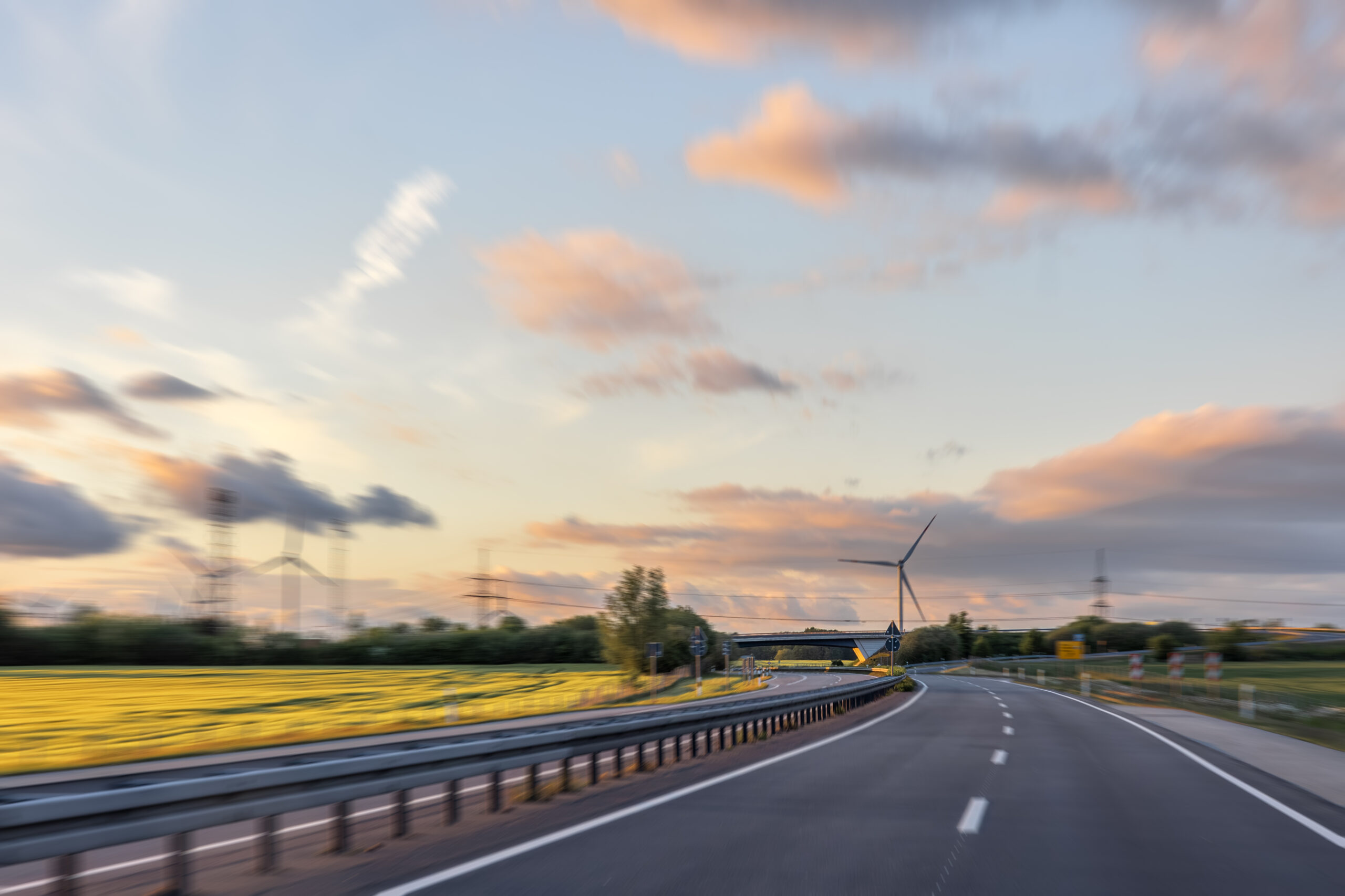 Snelweg tussen weilanden door met windmolens op de achtergrond